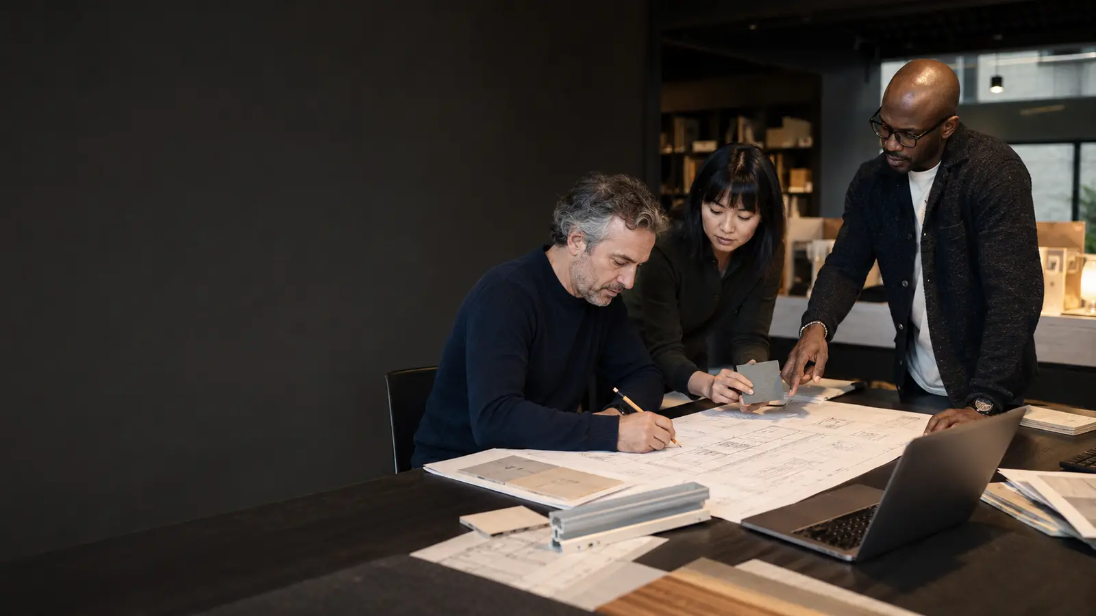 People reviewing architectural plans and linear lighting samples around a worktable.