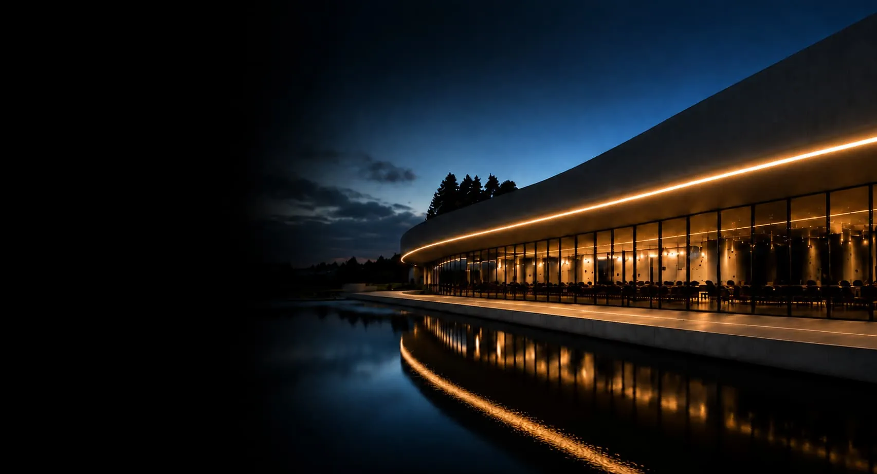 Warm linear light following a curved glazed facade beside reflecting water at dusk